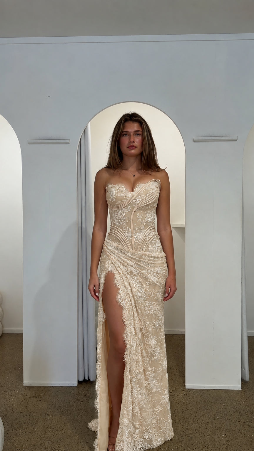 Woman wearing champagne cream strapless lace corset evening gown with high slit