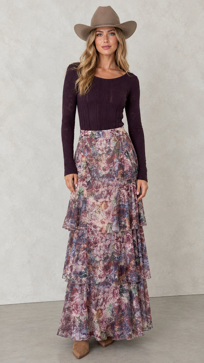 Front view of woman wearing Mauve Plum tiered floral maxi skirt with plum long sleeve top and hat