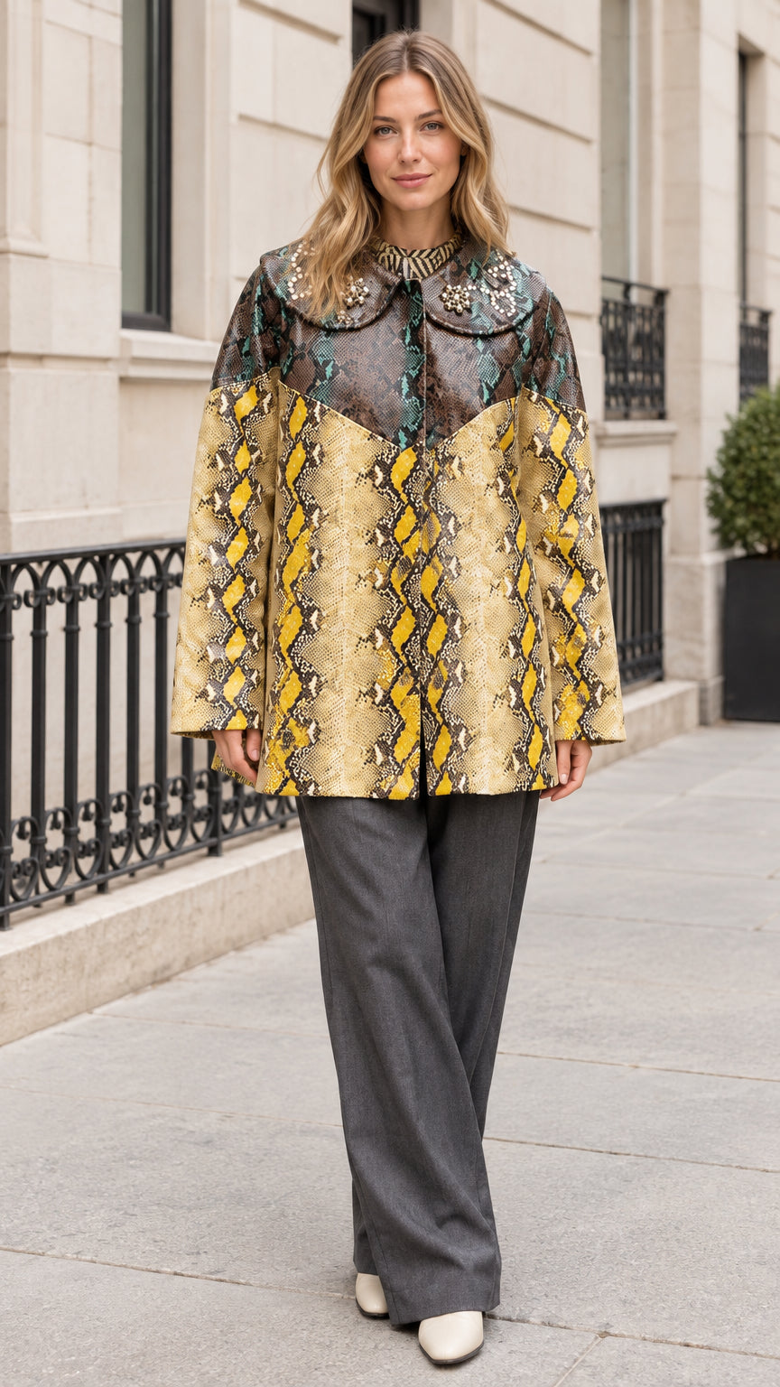 Front view of model wearing Teal Yellow snakeskin print coat with embellished collar and grey trousers