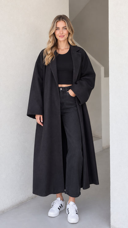 Full front view of a woman wearing the oversized black maxi longline coat with sneakers