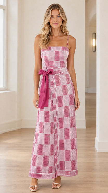 Front full view of woman wearing pink checkered spaghetti strap wide-leg jumpsuit with waist tie