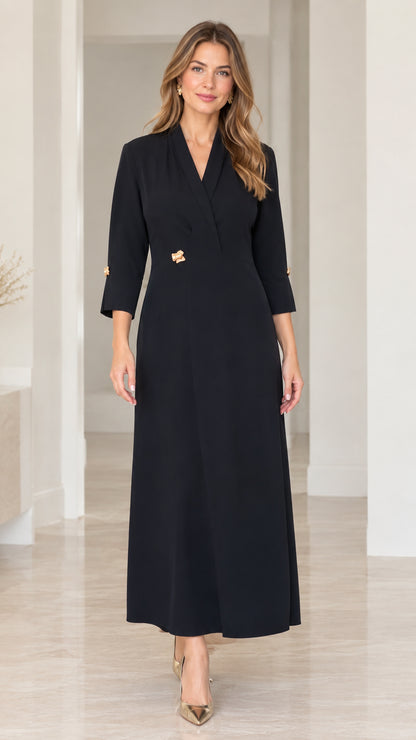 Front full-length view of woman in black lapel V-neck maxi dress with gold waist button
