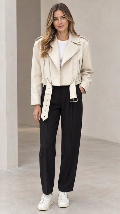 Front view of woman wearing cream cropped faux leather moto jacket with belt and black trousers