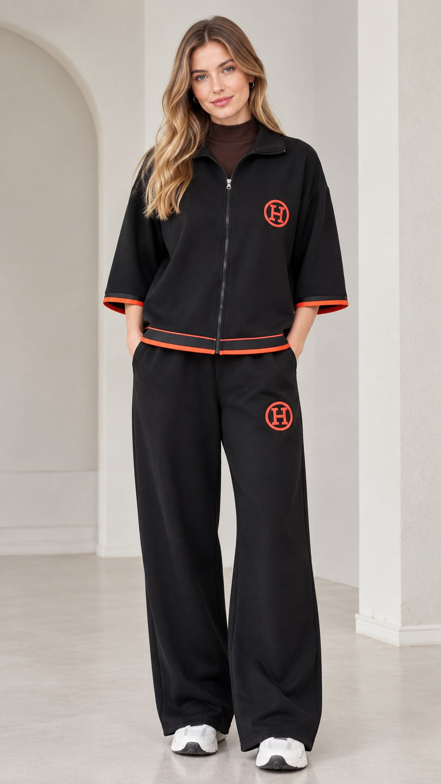 Front view of woman wearing black zip-up short sleeve tracksuit with wide leg pants and orange contrast trim