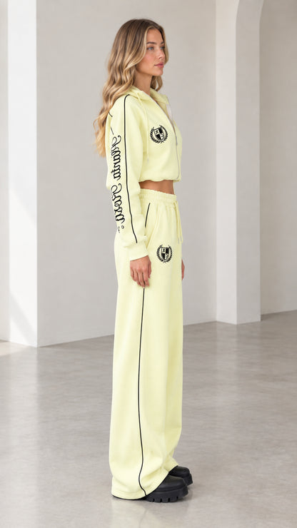 Side profile view of model in butter yellow tracksuit set showing sleeve embroidery and piping