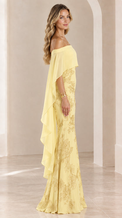 Side profile of woman wearing yellow floor-length formal dress with sheer cape overlay