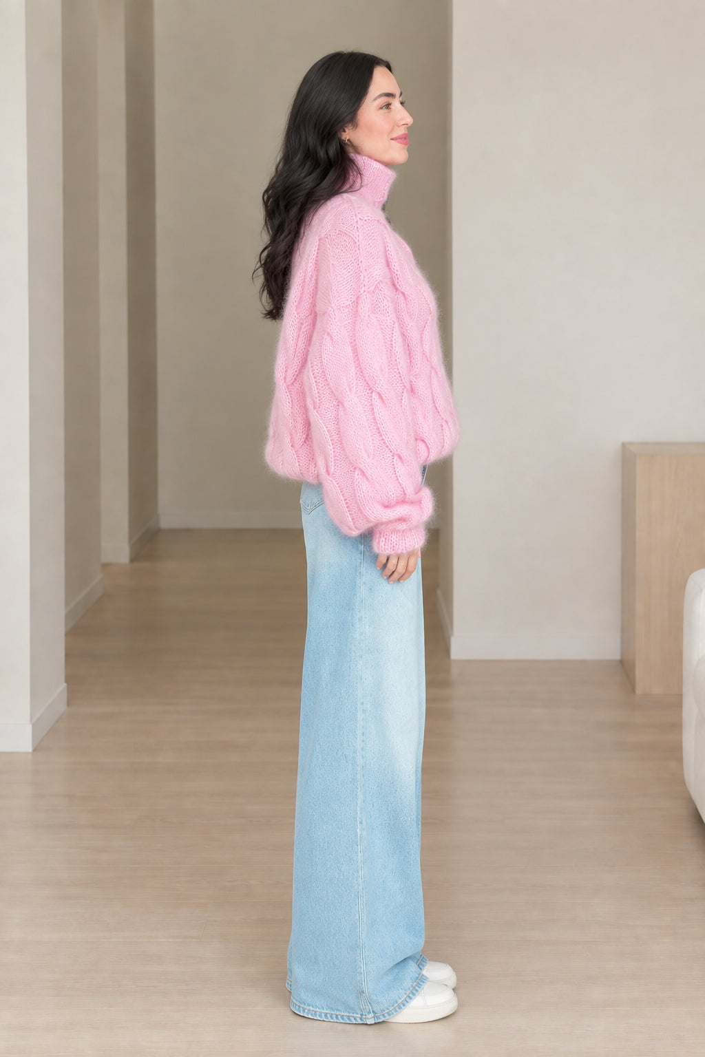 Side profile view of model wearing pink chunky cable knit turtleneck sweater