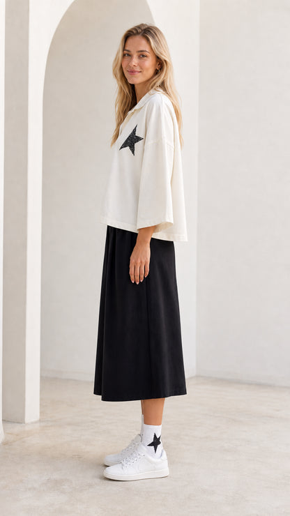 Side profile view of model wearing white star graphic collared top and black cropped pants