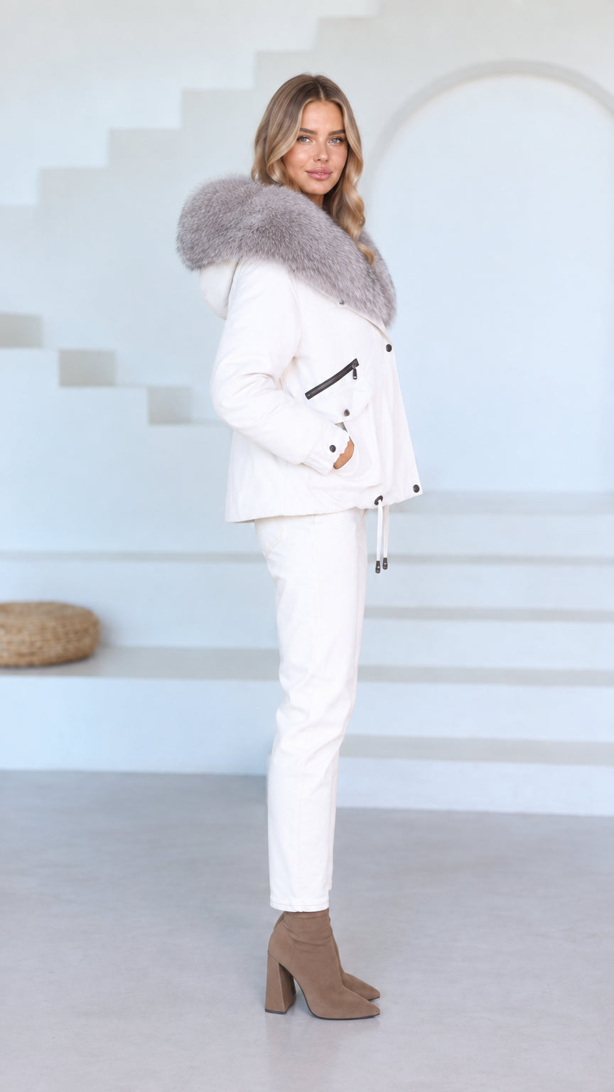 Side profile of model wearing white winter jacket and pants set with large fur hood