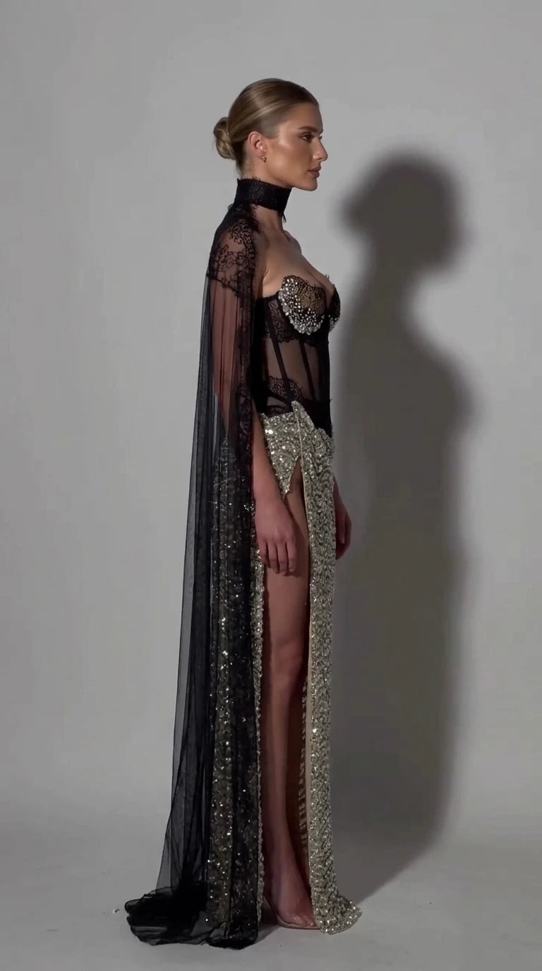 Side profile of model in silver sequin corset gown showing sheer back and floor-length cape