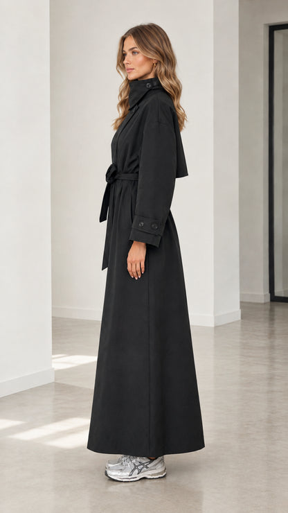 Side profile view of woman wearing long black belted trench coat with funnel collar