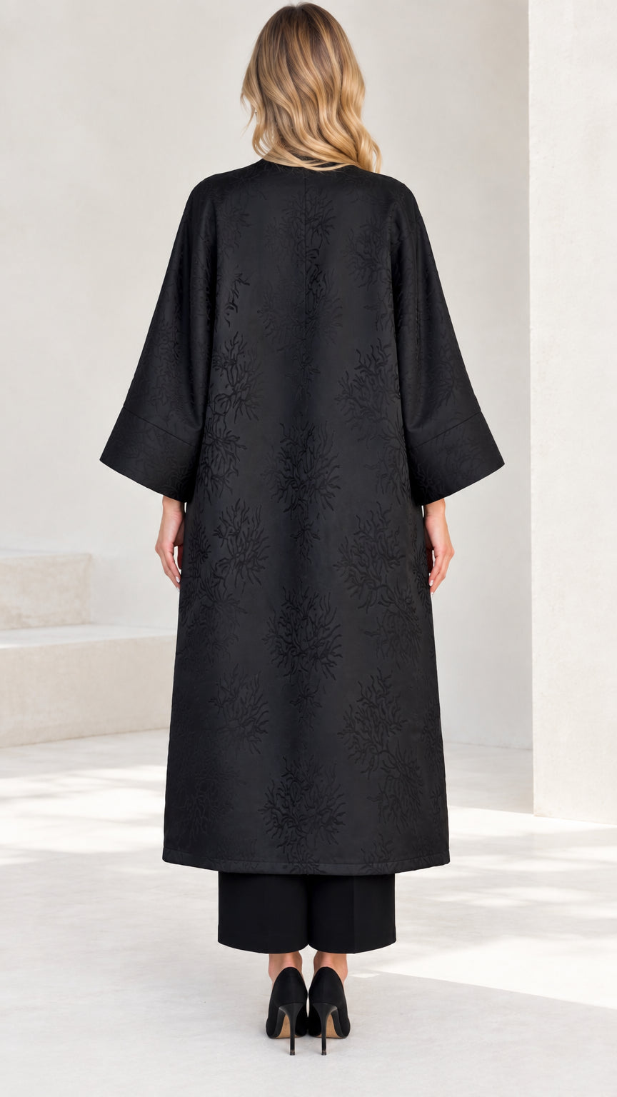 Back view of women's long black open front jacquard duster coat
