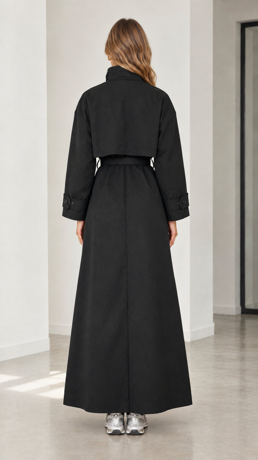 Back view of woman wearing full-length black trench coat with back storm flap detail