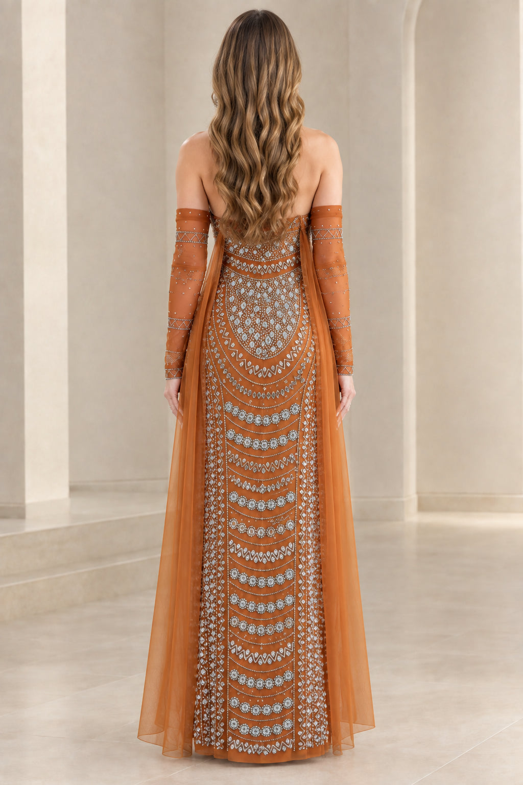 Back view of rust orange beaded formal evening gown with long sheer cape details