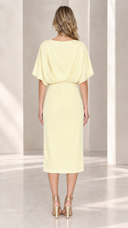 Back view of model in pale yellow midi dress showing draped back and sleek skirt