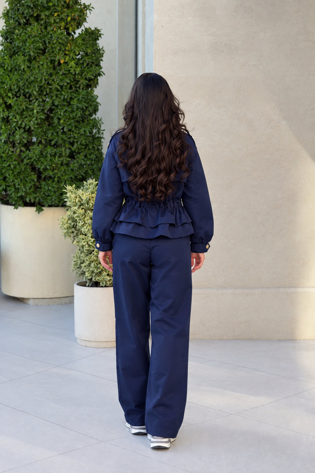 Back view of model wearing Navy Blue matching jacket and pant set with ruffled peplum hem