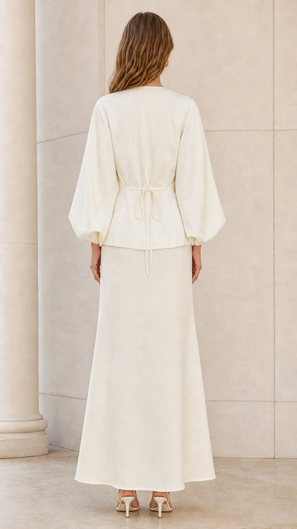 Back view of model wearing ivory lantern sleeve top with back waist tie and matching maxi skirt