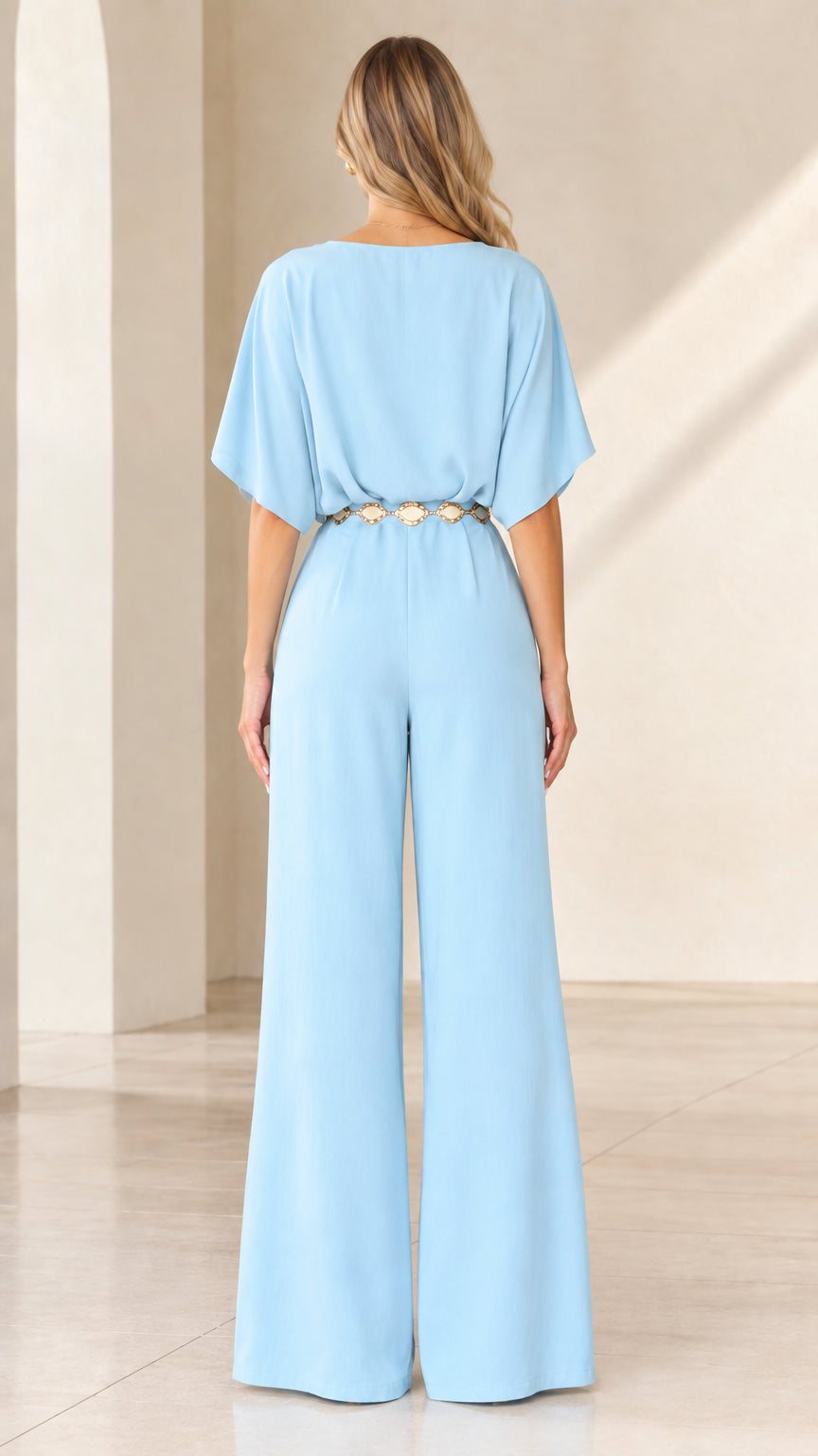 Back view of woman in light blue wide-leg jumpsuit with waist belt