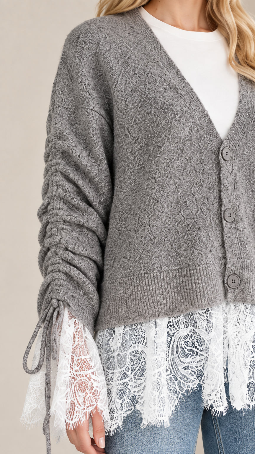 Close-up detail shot of grey knit cardigan showcasing ribbed buttons, ruched sleeve ties, and white eyelash lace