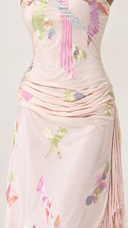 Close-up detail of blush pink dress showing gathered fabric, abstract motif, and fringe trim