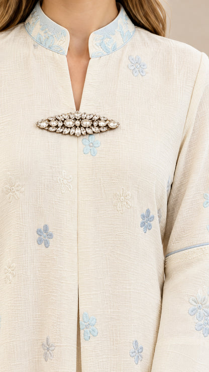Close-up detail of textured fabric, embroidered split collar, and crystal brooch accent