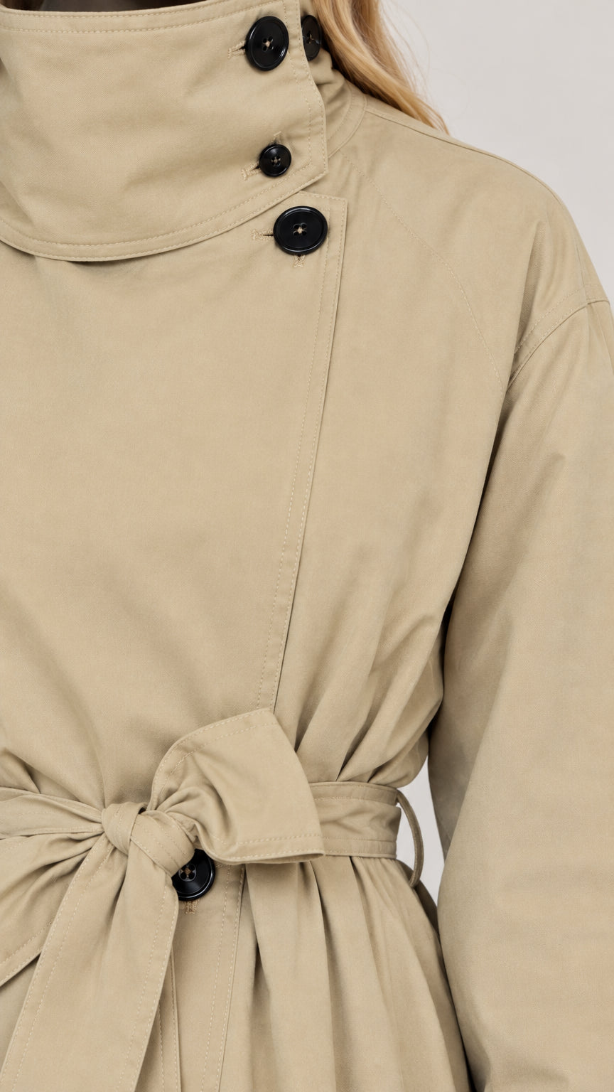 Close-up detail of beige trench coat collar buttons and waist belt