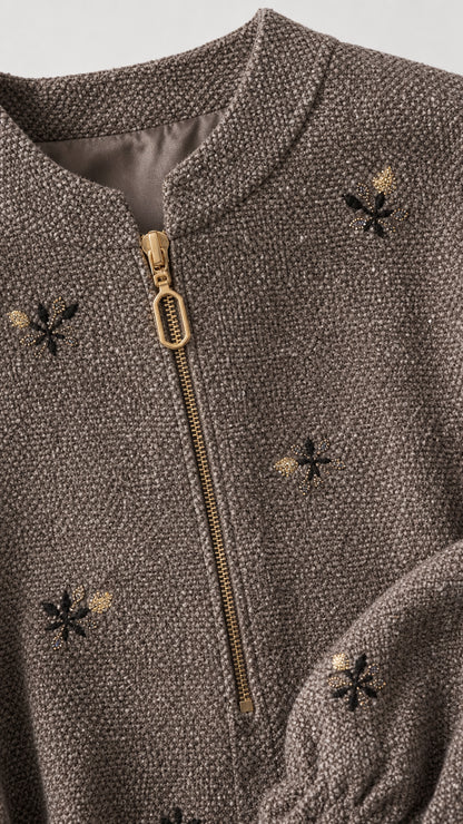 Close-up detail of taupe textured fabric, zipper, and floral embroidery