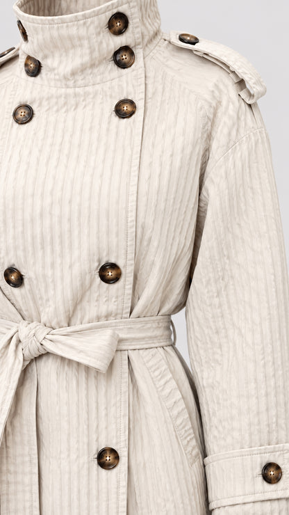 Close-up detail of cream textured short coat showing double-breasted buttons, collar, and belt