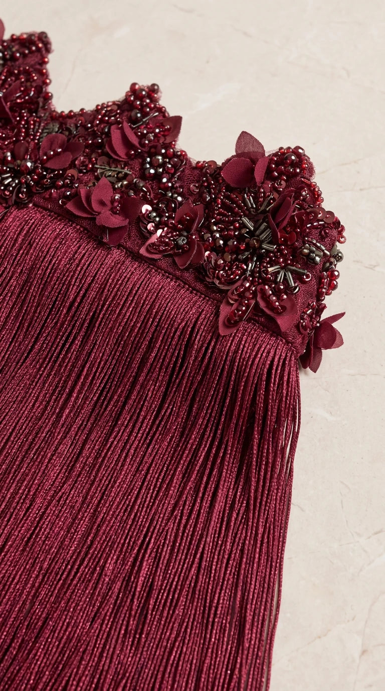 Close-up detail of beaded floral appliqués and textured fringe on burgundy evening dress