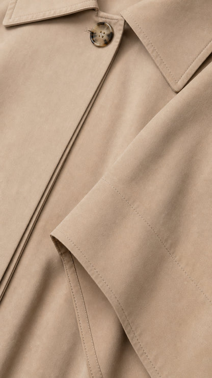 Close-up detail of beige cape collar, tortoiseshell button, and neat seam stitching