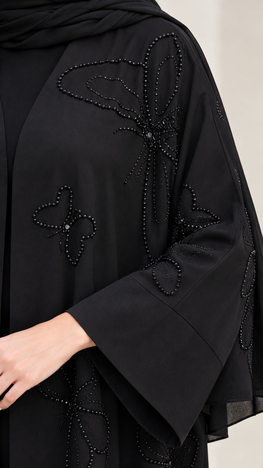 Close-up detail of tonal beaded butterfly motifs and flared cuffs on black abaya
