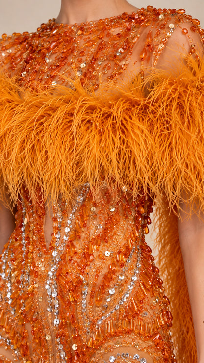 Close-up detail of intricate beadwork, sequins, and feather trim on orange evening gown