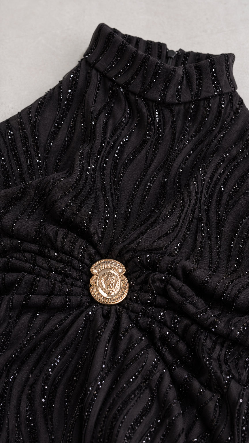 Close-up detail of wavy glitter pleated fabric and ornate gold waist crest button