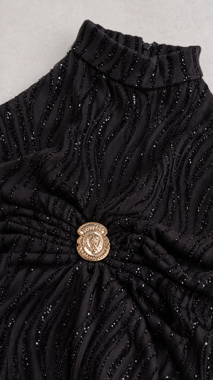 Close-up detail of wavy glitter pleated fabric and ornate gold waist crest button