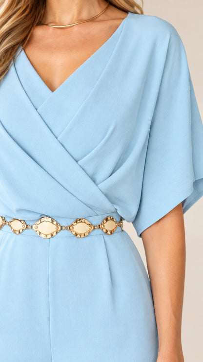 Close-up detail of light blue jumpsuit showing wrap neckline and gold chain belt