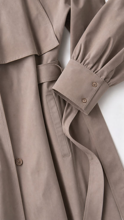 Close-up detail of the taupe brown coat fabric, belted waist, and tailored double-button sleeve cuff