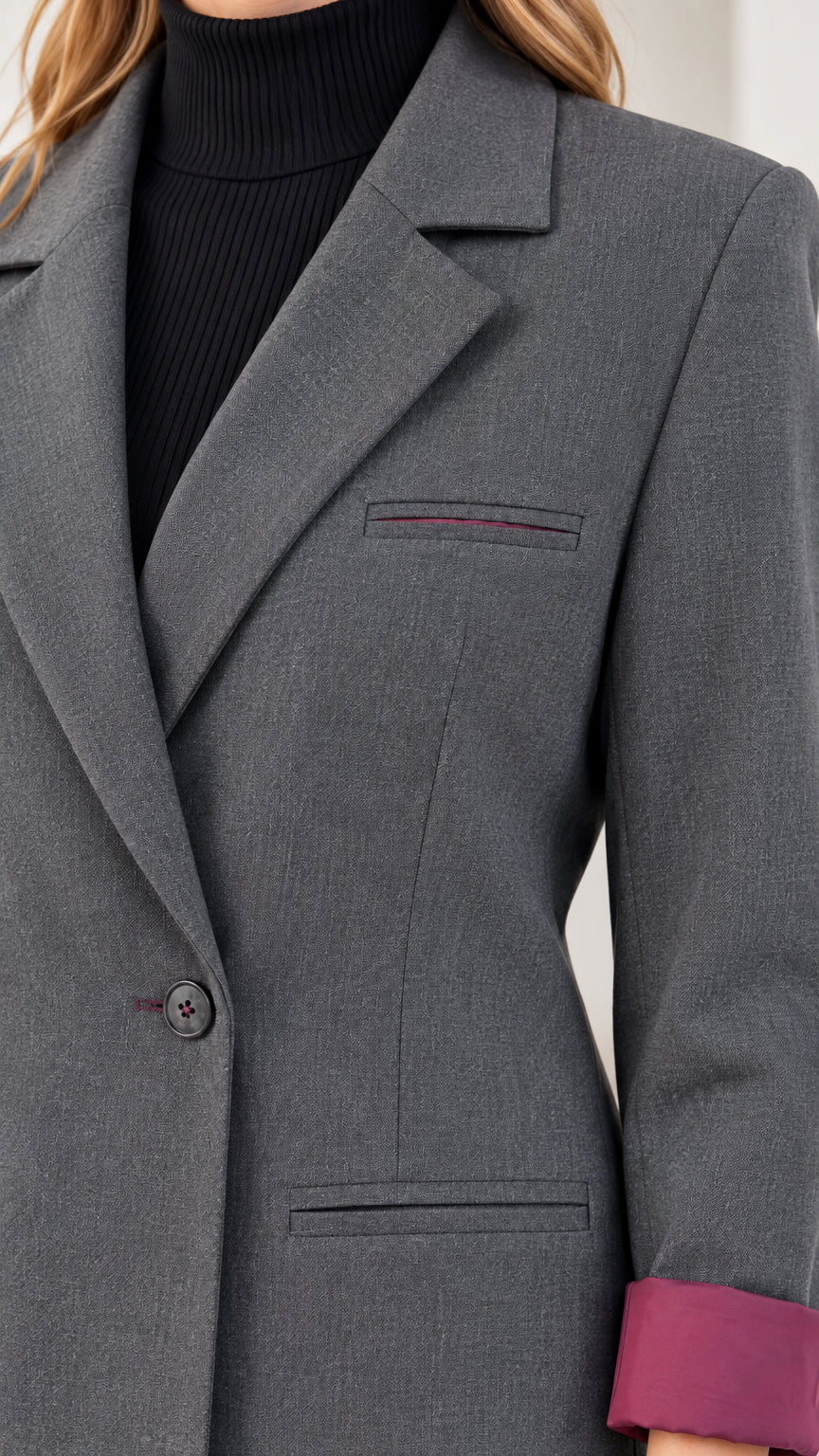 Close-up detail of charcoal grey blazer notched lapel, welt pocket, and contrast cuff