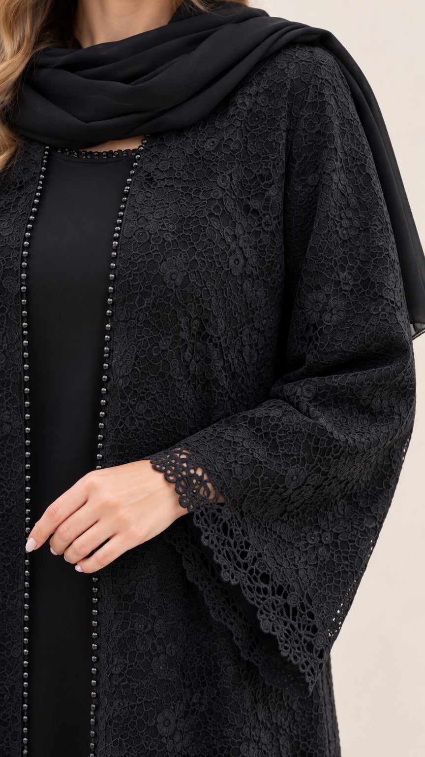 Close-up detail of black floral lace fabric, scalloped sleeve hem, and beaded front trim