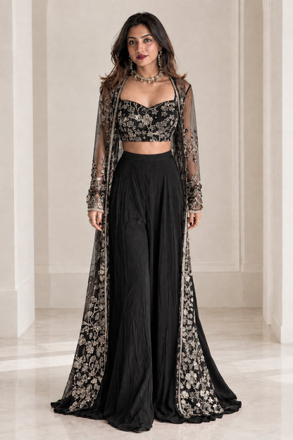 Model wearing black embroidered sweetheart crop top and wide-leg palazzo set with sheer cape