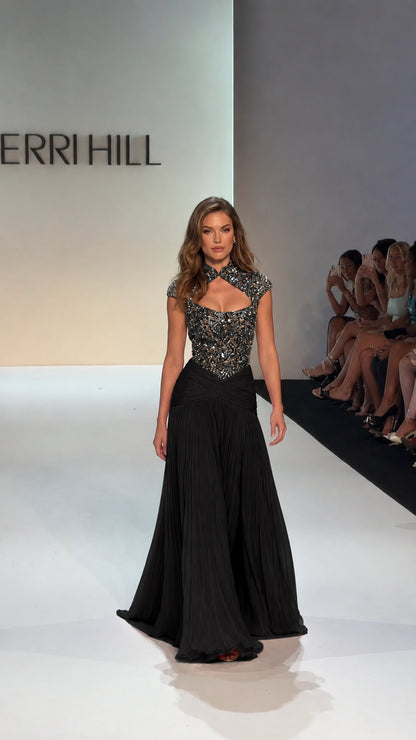Model walking runway in Black embellished bodice pleated evening gown