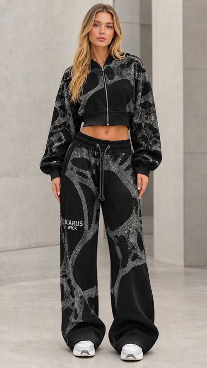 Model wearing black cropped zip hoodie and wide-leg sweatpants set with silver glitter detailing