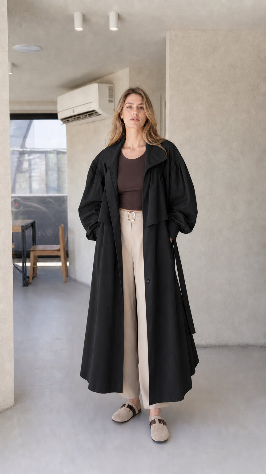 Model wearing black oversized maxi trench coat paired with cream wide-leg trousers