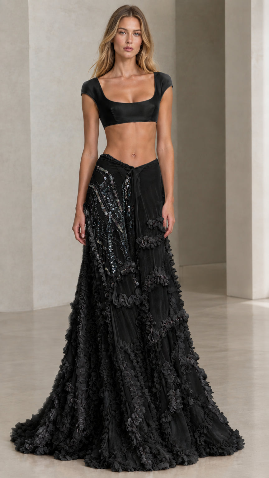 Front view of model wearing black two-piece satin crop top and ruffled evening skirt