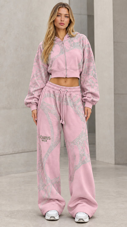Model wearing light pink cropped zip hoodie and wide-leg sweatpants set with glitter graphics