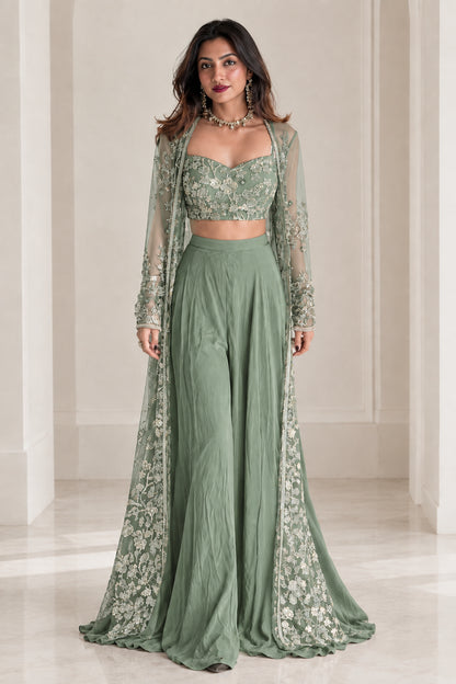 Model wearing sage green embroidered crop top and wide-leg trousers with floor-length sheer cape