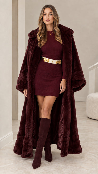 Full front view of burgundy hooded maxi faux fur coat styled over matching wine knit dress