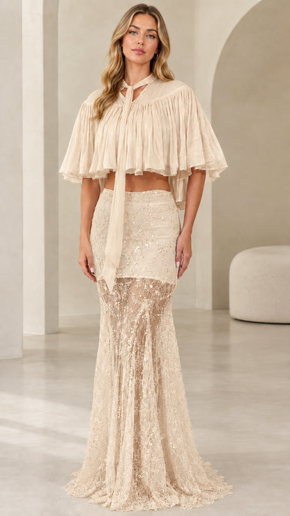 Model wearing champagne beige sequin lace two-piece formal dress with capelet overlay